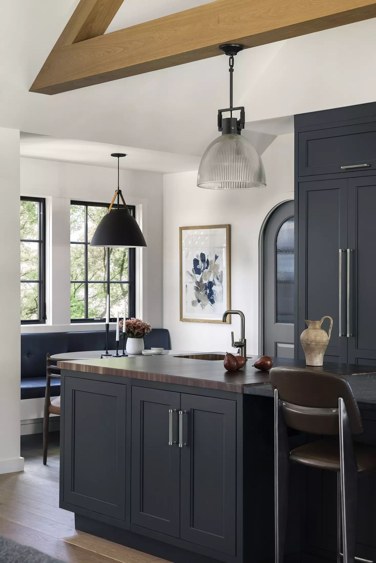 Kitchen with dark cabinetry, wood countertops, island, two light fixtures, and seating with cushions.