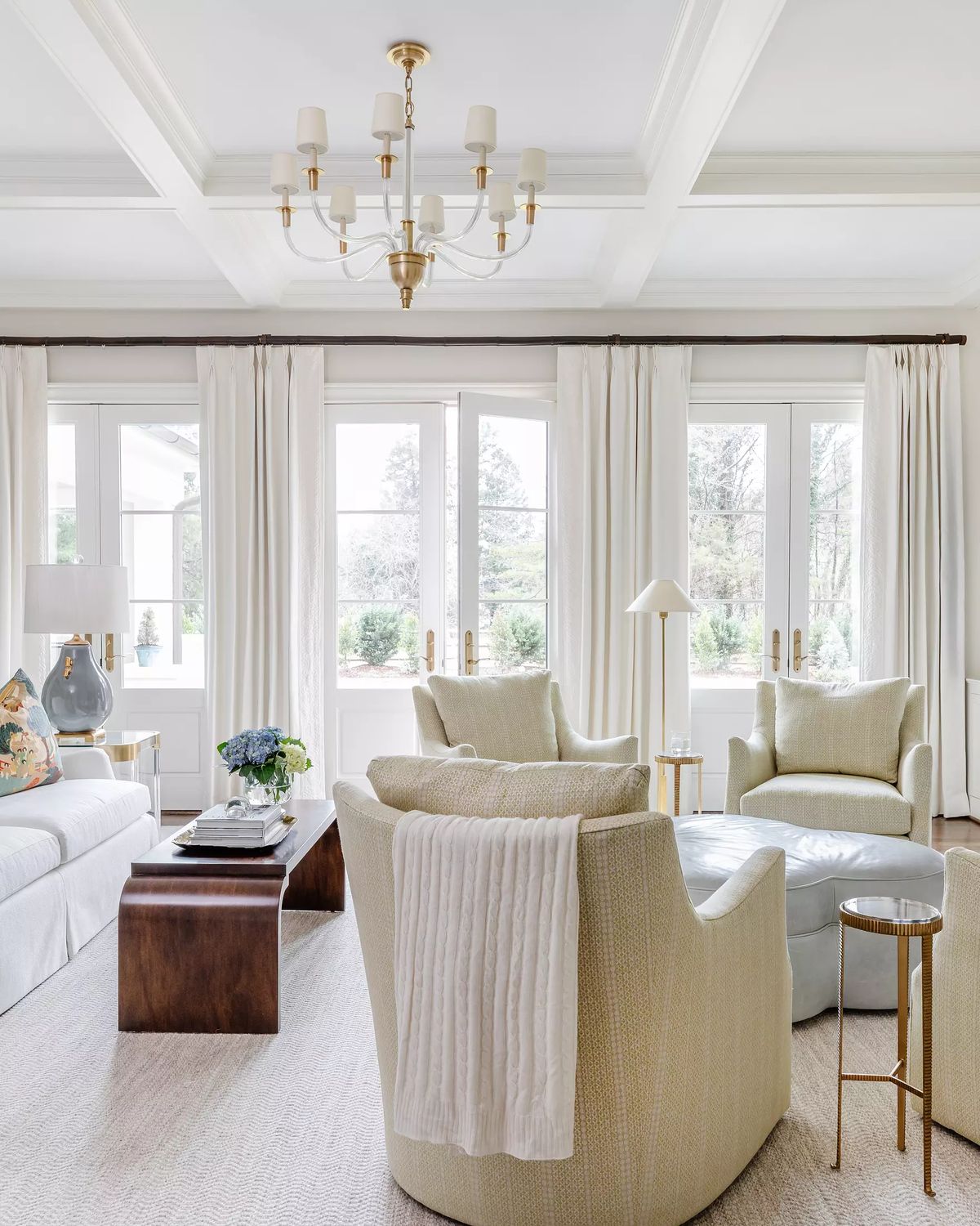 Living room with white sofa, gray chairs, wood coffee table, large windows, and coffered ceiling.
