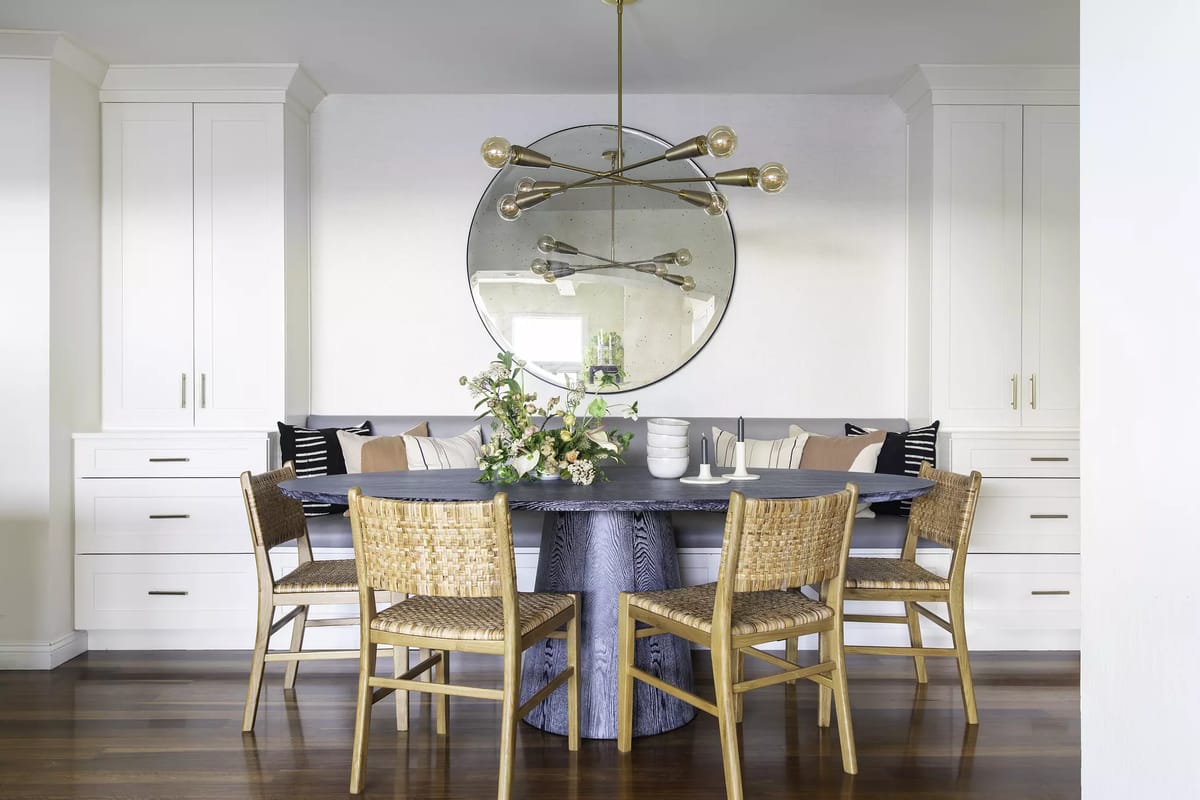Dining room with round table, woven chairs, built-in cabinetry, large mirror, and decorative flowers.