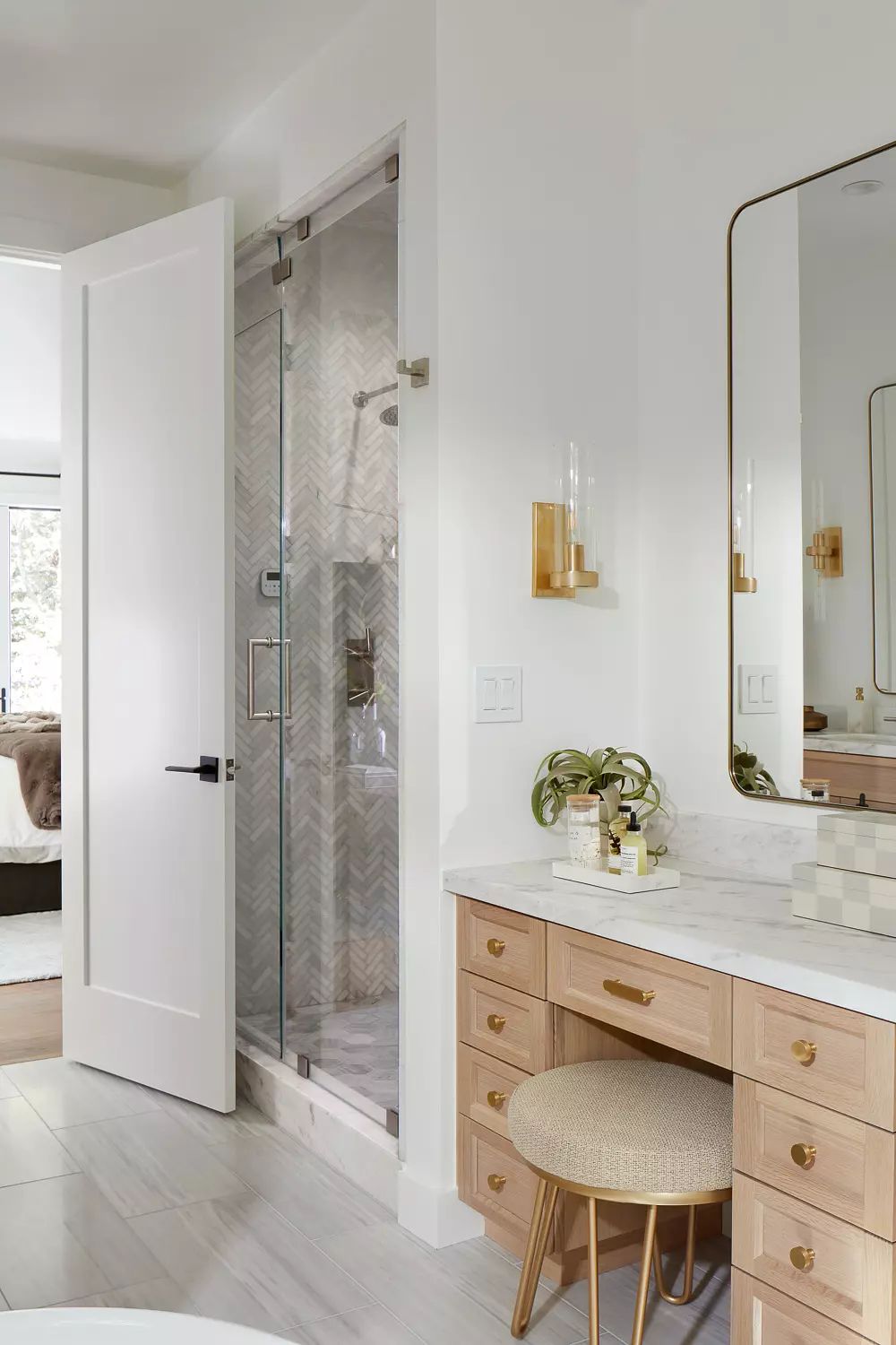 Bathroom with glass shower, wooden vanity, marble countertop, round mirror, and wall-mounted sconces.