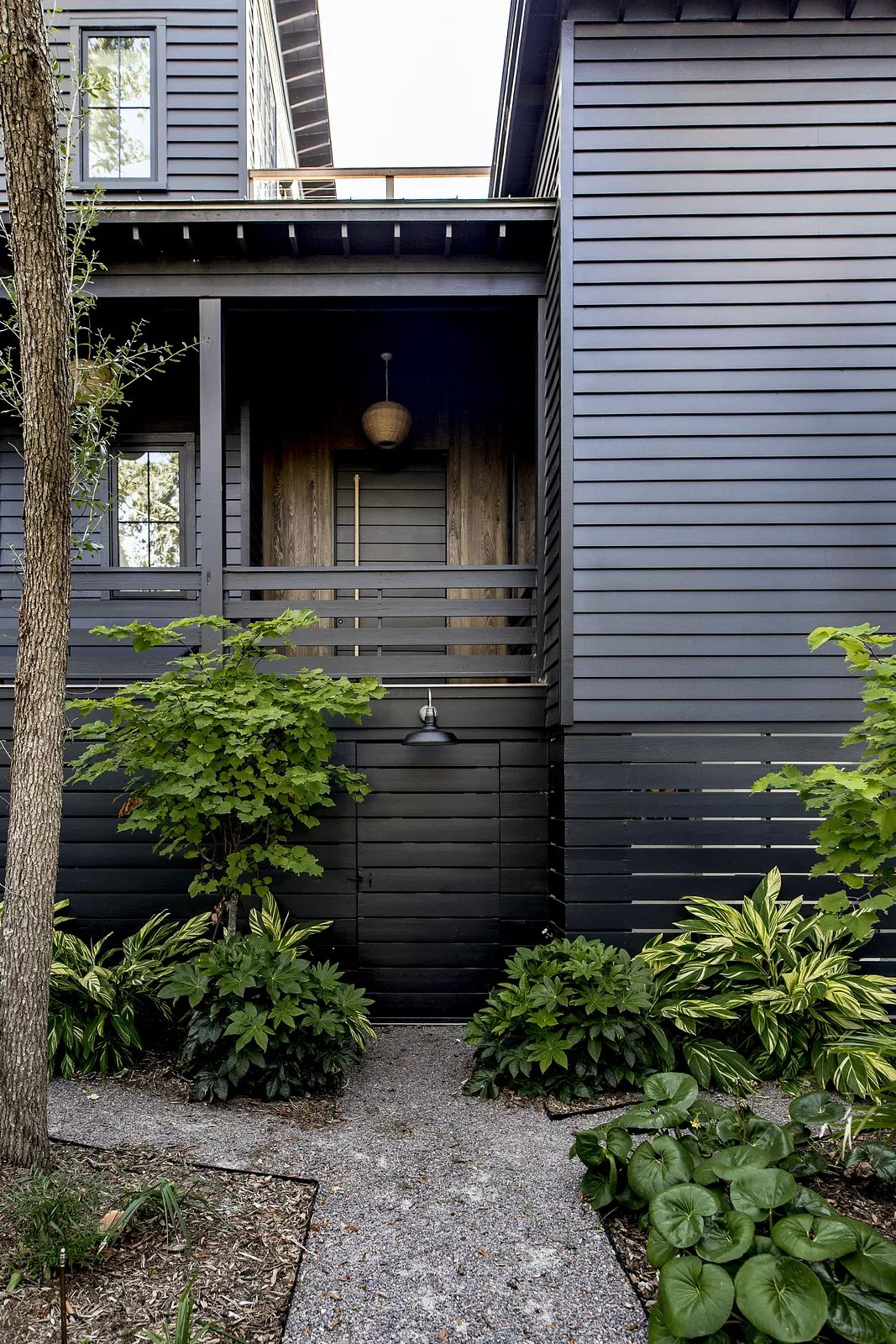 Exterior front with wooden door, gravel pathway, shrubs, and ceiling-mounted fixture above the entrance.