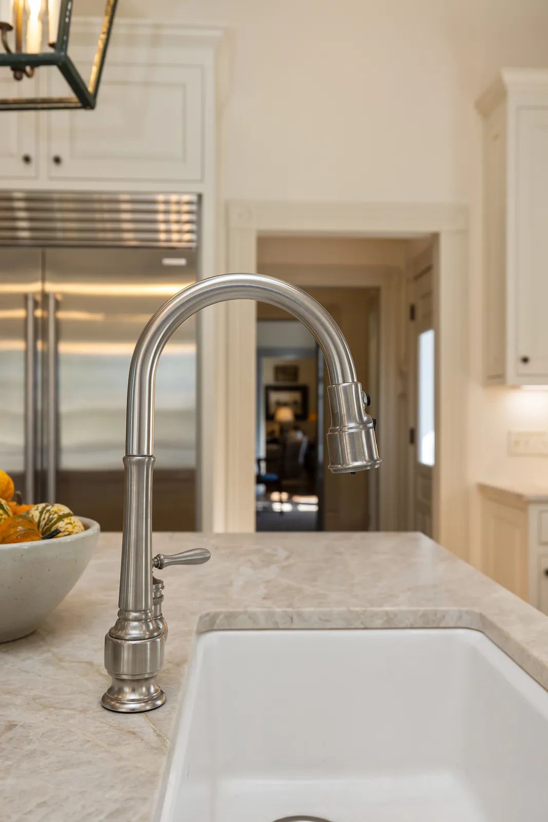Kitchen with stainless steel faucet, white sink, light countertops, and a bowl of fruit.