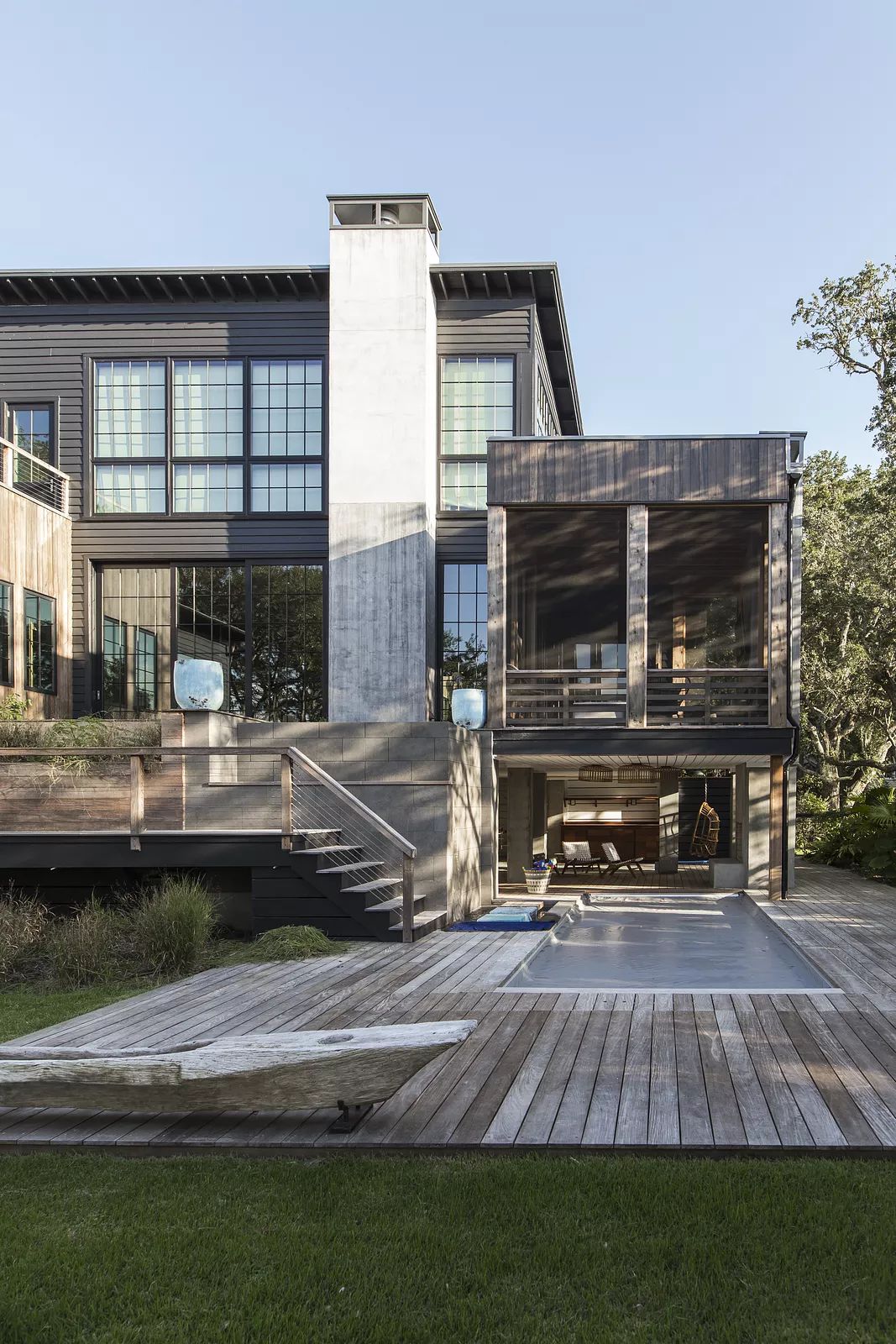 Exterior rear view of a two-story house with large windows, wooden decks, and a swimming pool area.