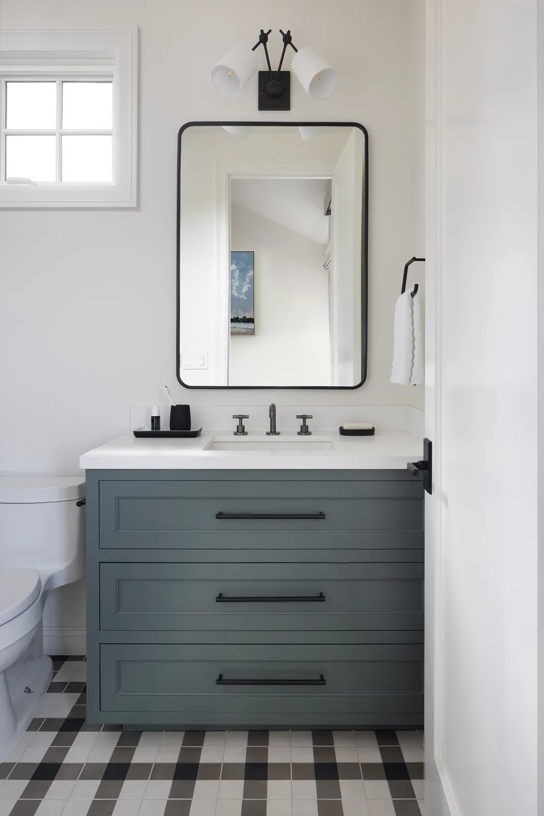 Bathroom with grey cabinet, white sink, black faucet, and black and white tiled floor.