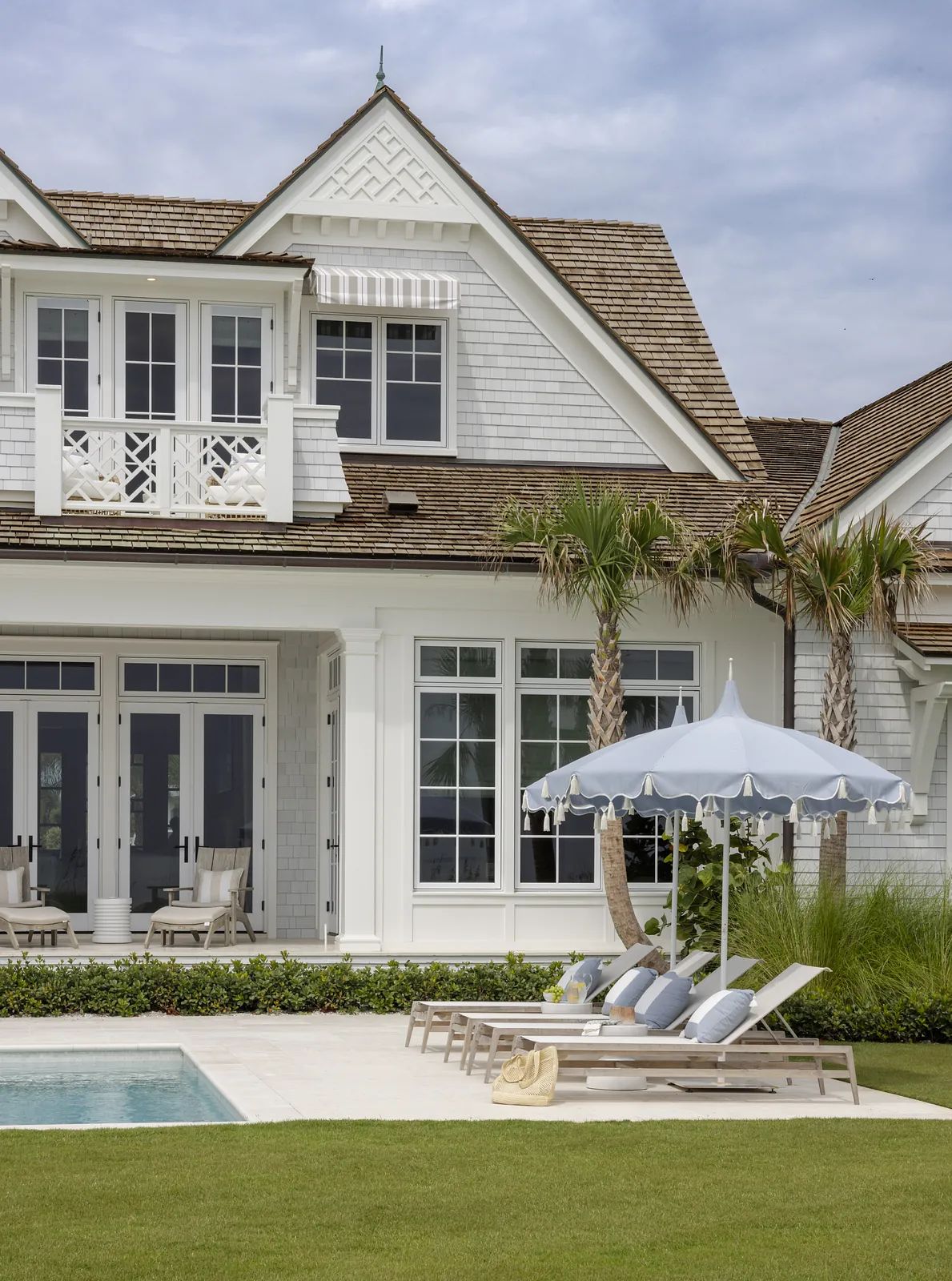 Exterior rear view of a house with pool, loungers, patio umbrella, and landscaped grass.