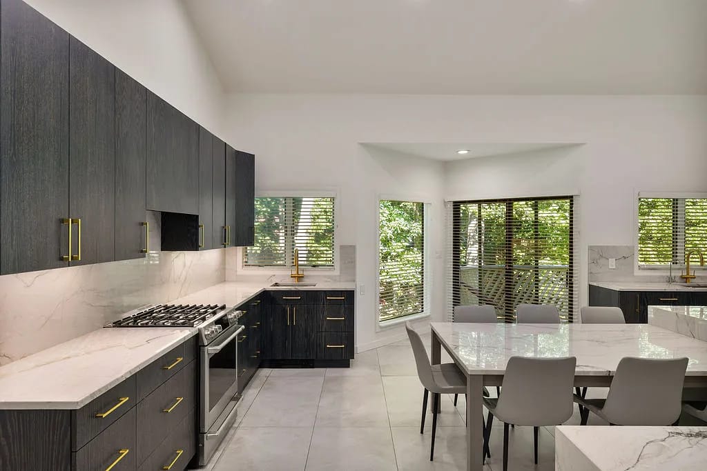 Kitchen with dark wood cabinets, marble countertop, stainless steel appliances, and dining table with gray chairs.
