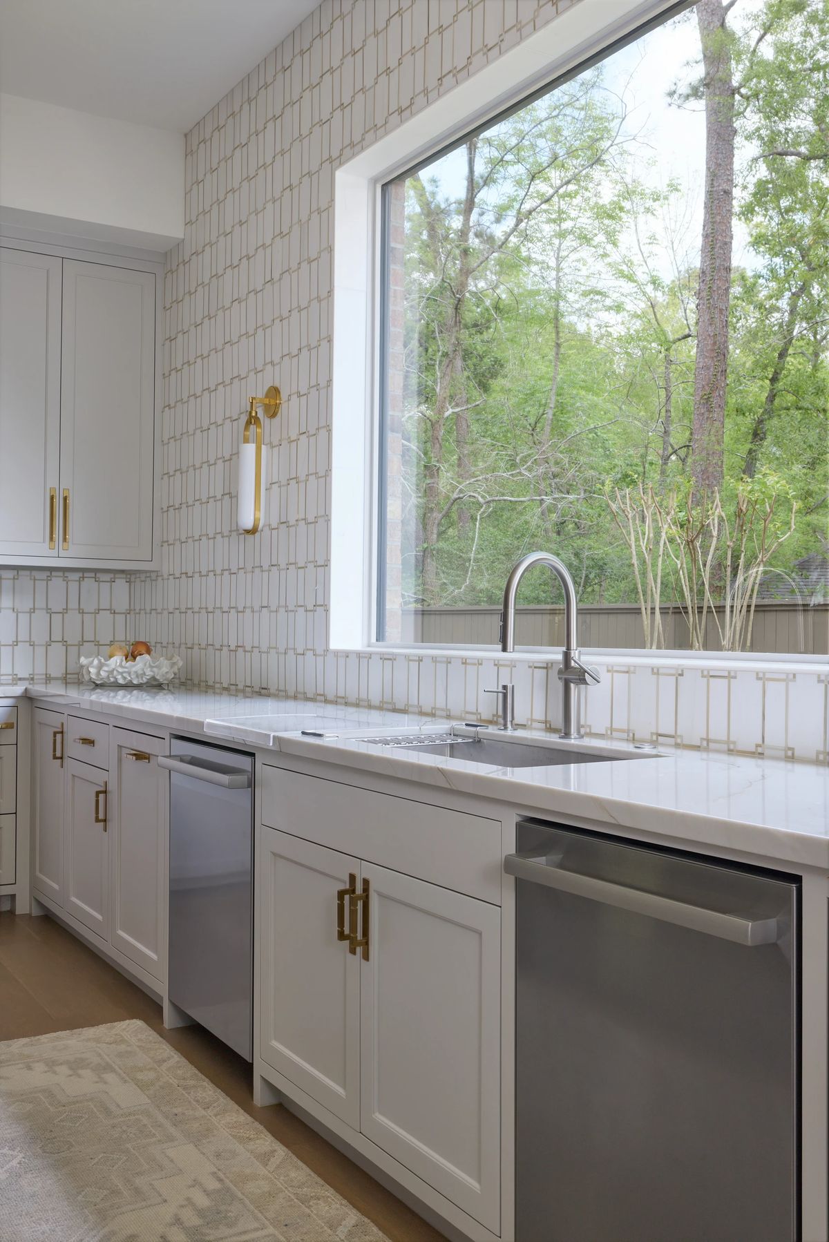 Kitchen with white cabinets, stainless steel sink, dishwasher, light stone countertop, and large window.