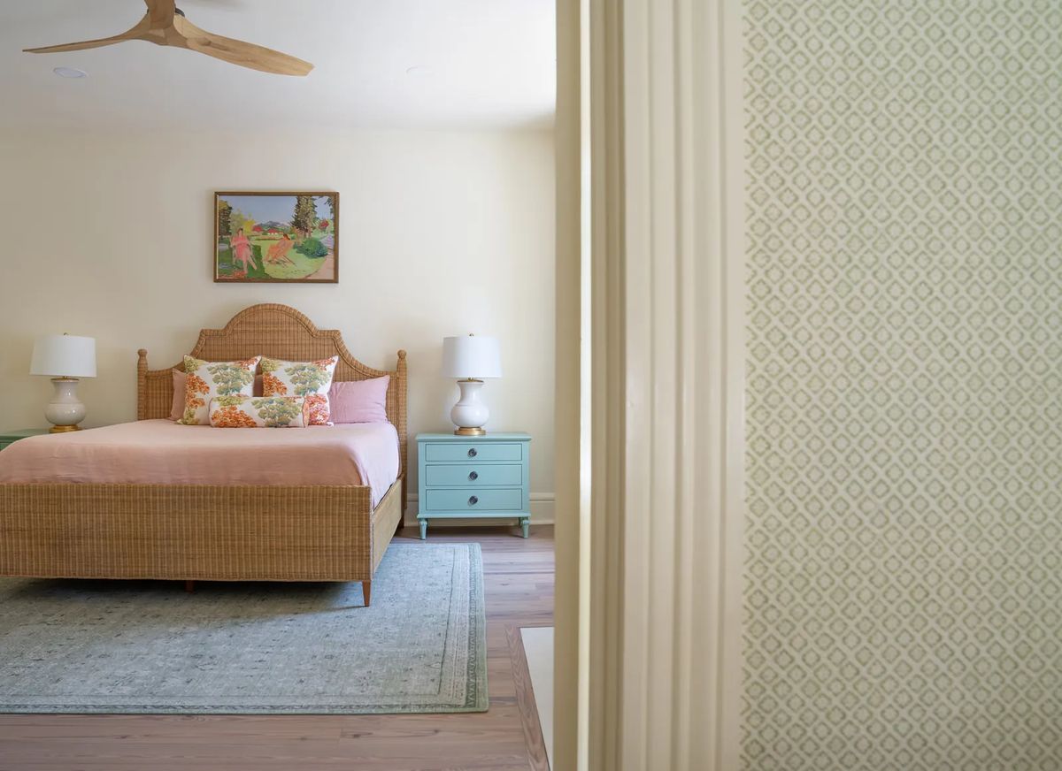 Bedroom with rattan headboard bed, nightstands, lamps, area rug, and a wall painting.