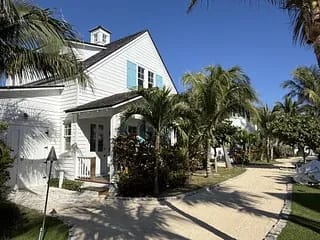 Front exterior view of a house with white siding, blue shutters, and palm trees.