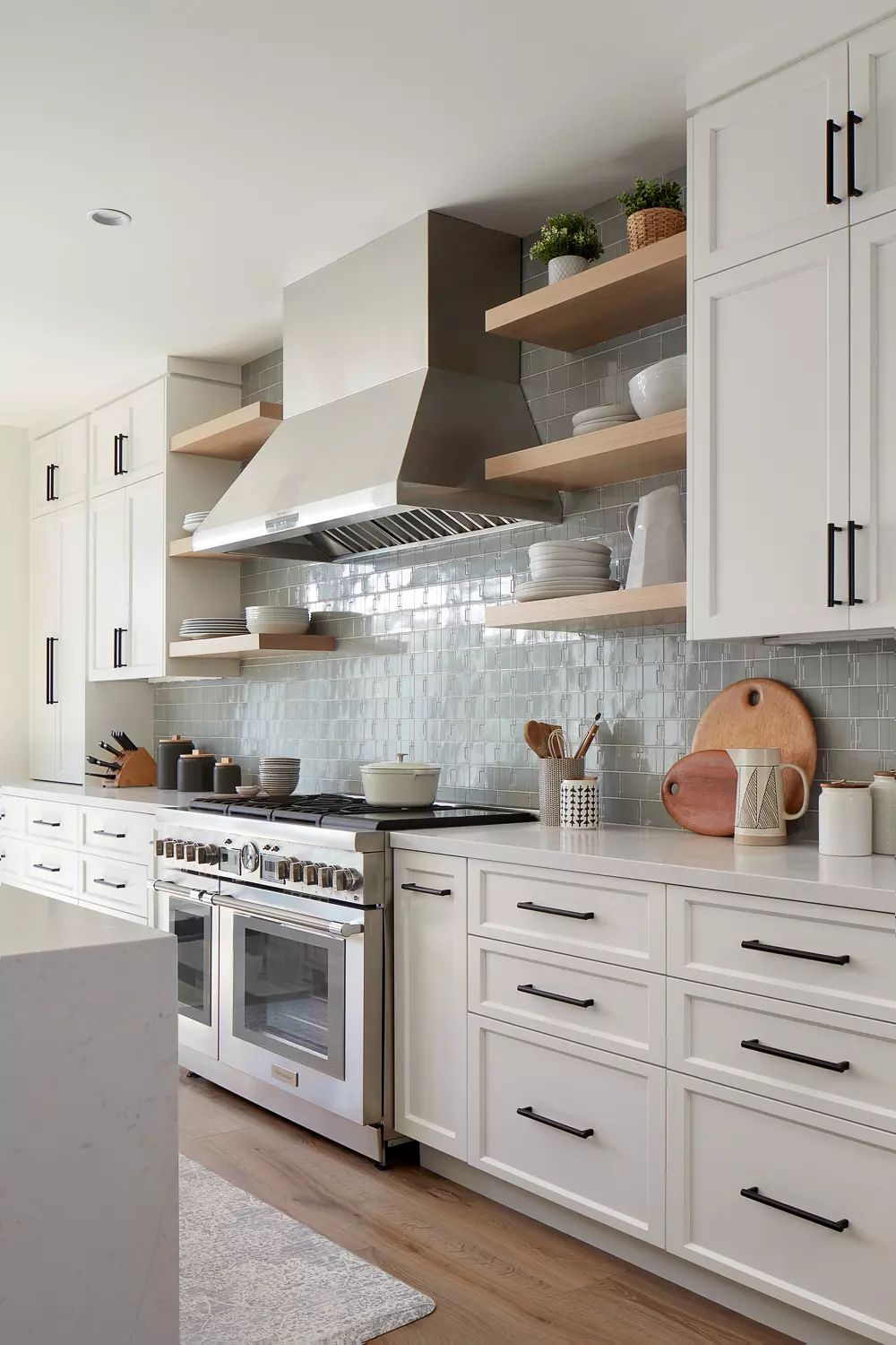 Kitchen with white cabinetry, stainless steel range hood, island, open shelving, and gray tile backsplash.