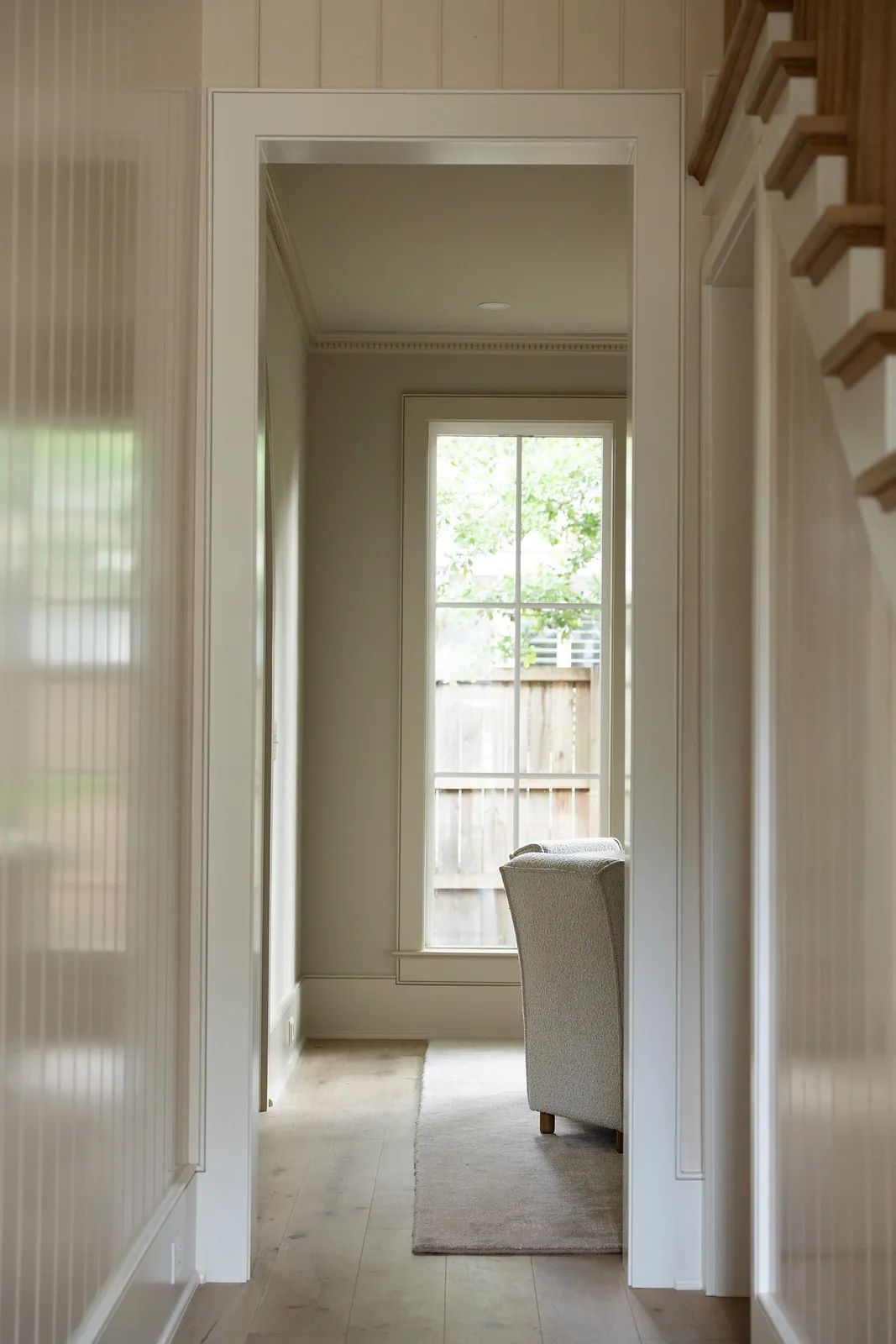 Hallway with walls, large window, beige chair, rug, crown molding, and wooden staircase.