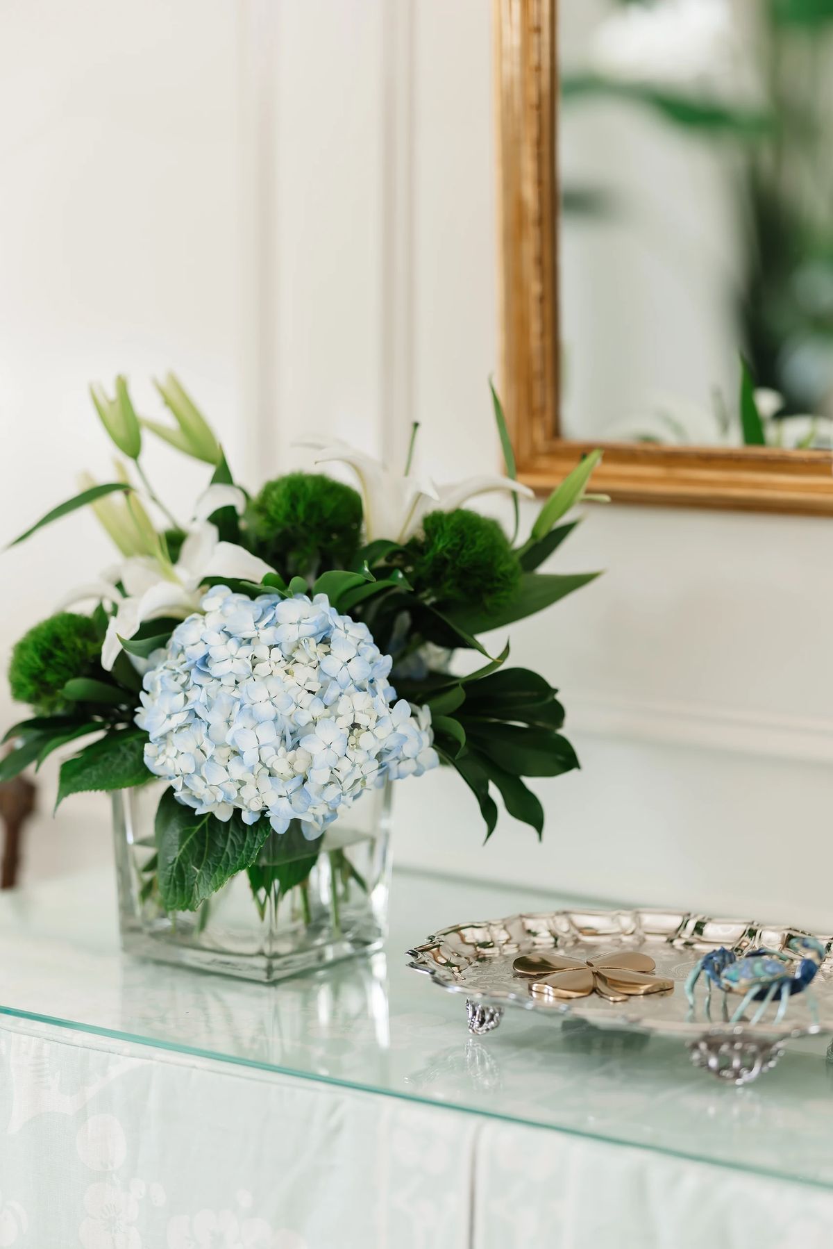 Decorative display with glass vase of flowers, gold mirror, and silver tray with accessories.