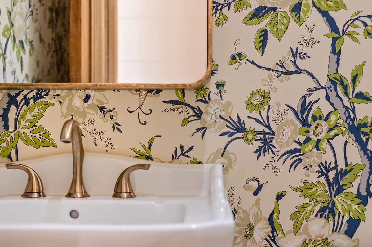 Bathroom with white sink, bronze faucets, floral wallpaper, and gold-framed mirror.