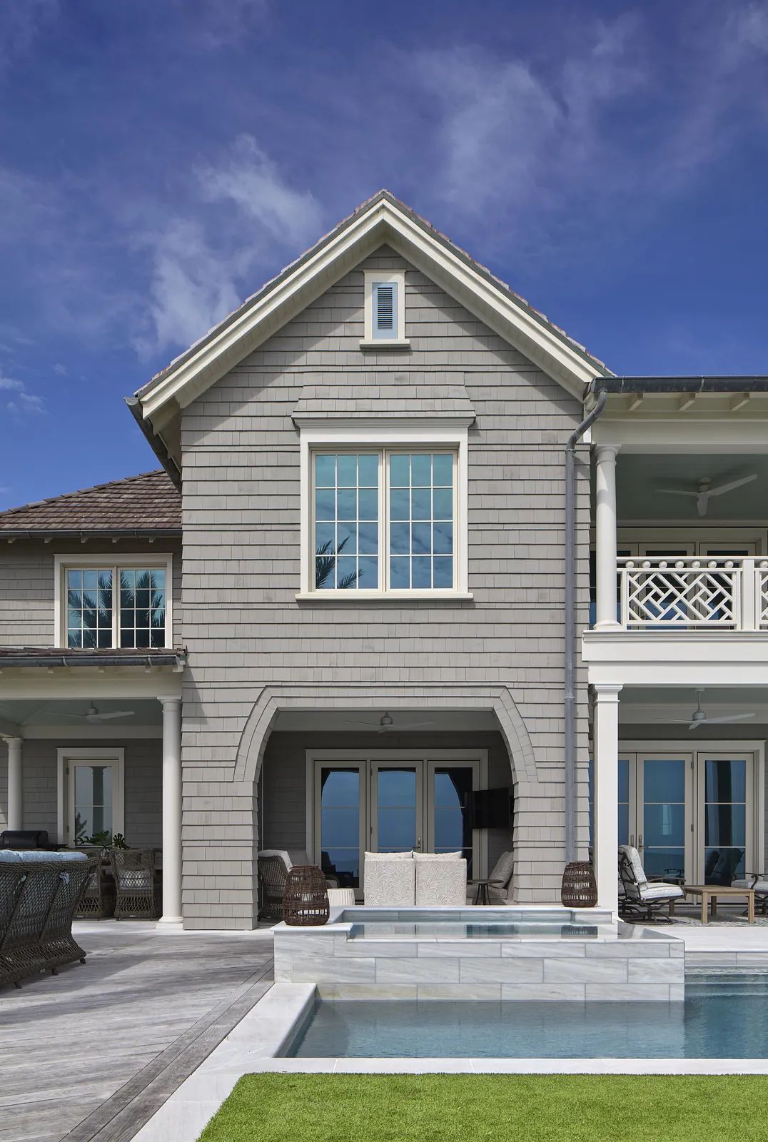 Exterior rear view with gray siding, large windows, sliding glass door, patio, swimming pool, and grass.