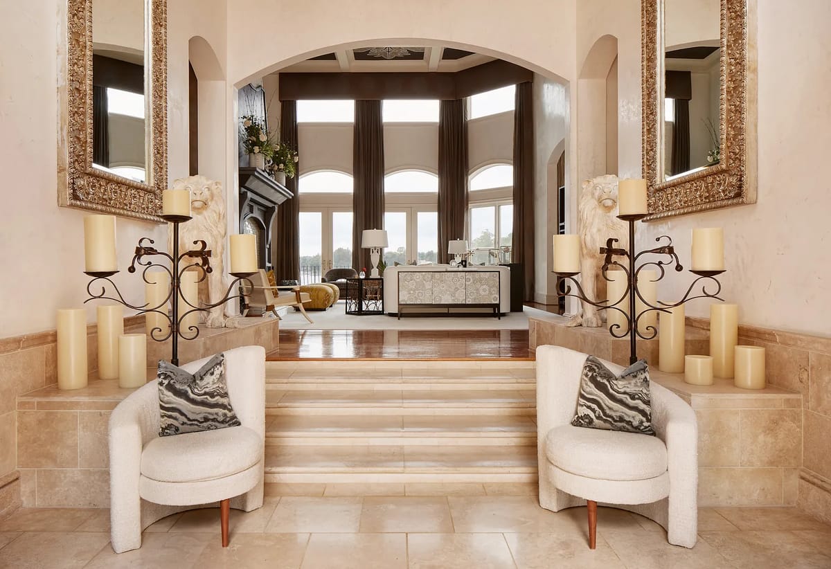 Foyer with two upholstered chairs, mirrors, candle holders, and a view of the living area with windows.