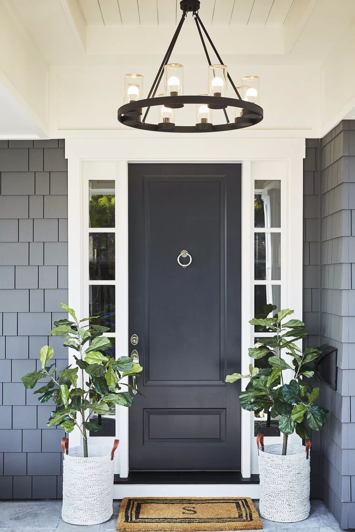Exterior front entrance with black door, windows, potted plants, welcome mat, and round chandelier