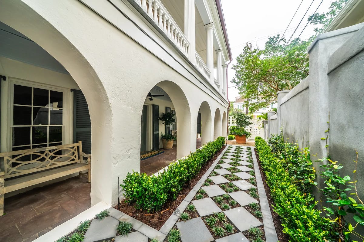 Exterior front with paved pathway, arches, plants, and a bench leading to a porch.