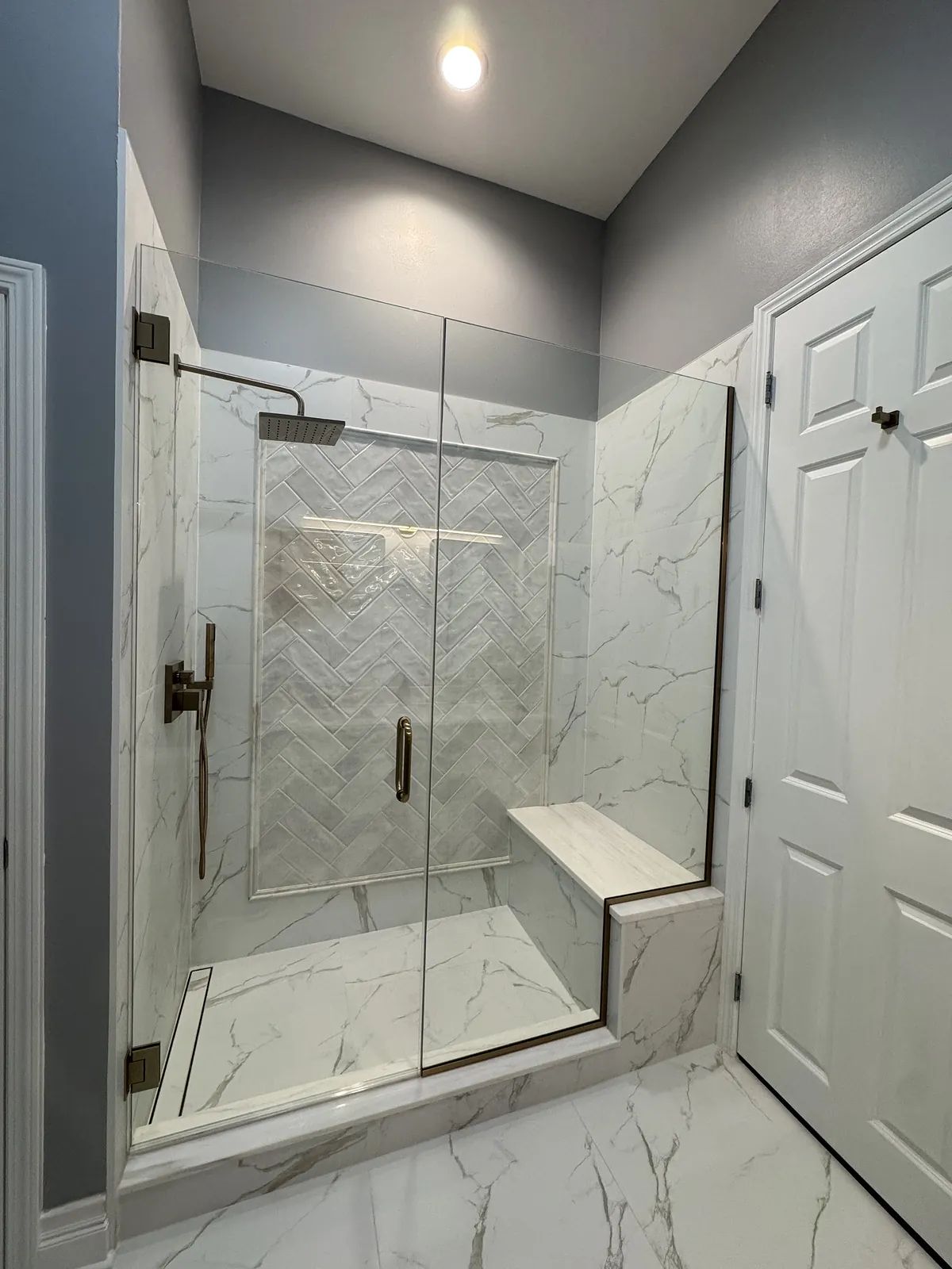 Bathroom with glass shower enclosure, herringbone tiled wall, and marble tile flooring.