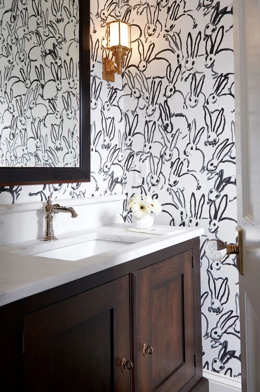 Bathroom with marble countertop sink, dark wood vanity, bunny motif wallpaper, and wall-mounted sconce