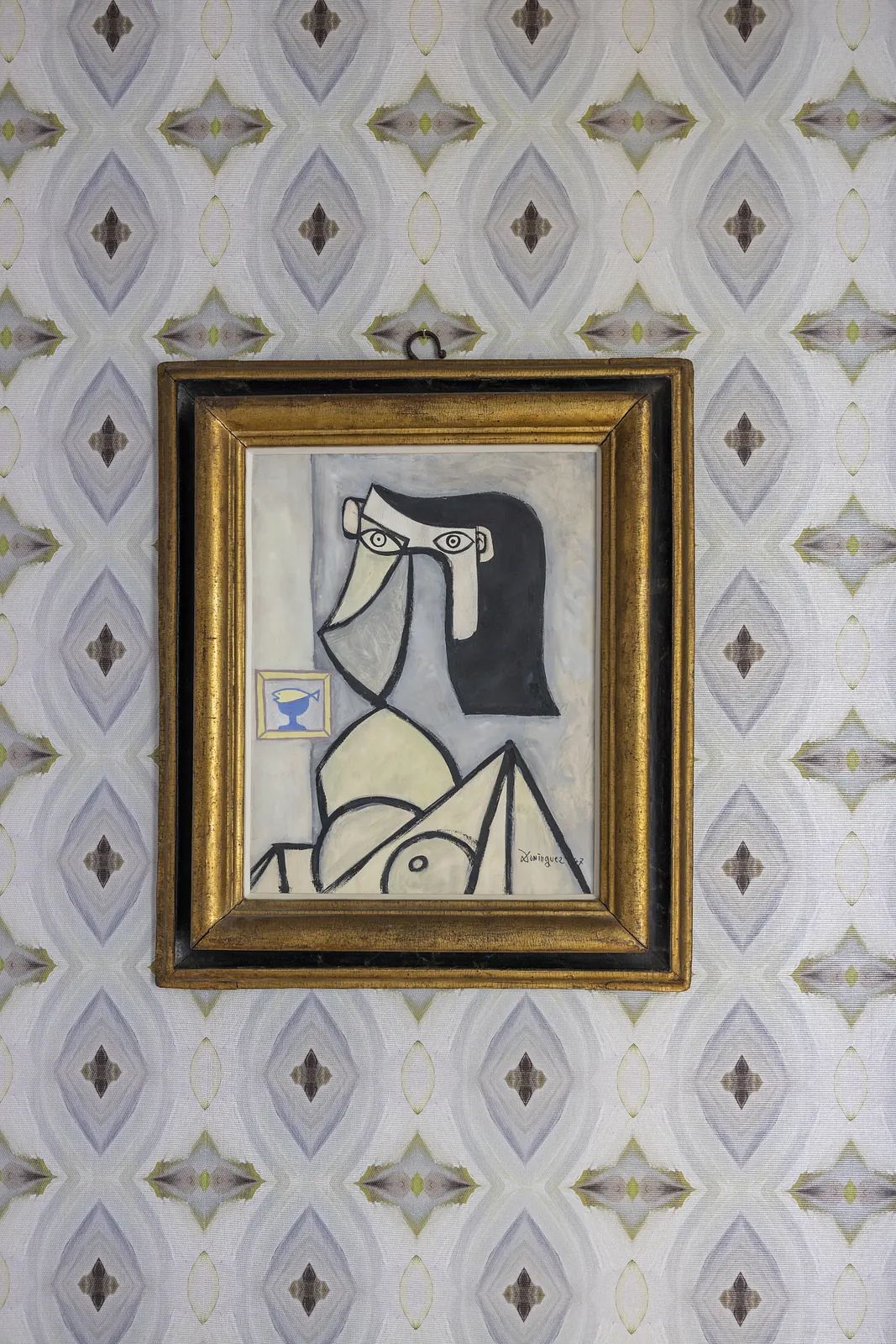 Framed abstract artwork on patterned wallpaper with geometric design in neutral tones.