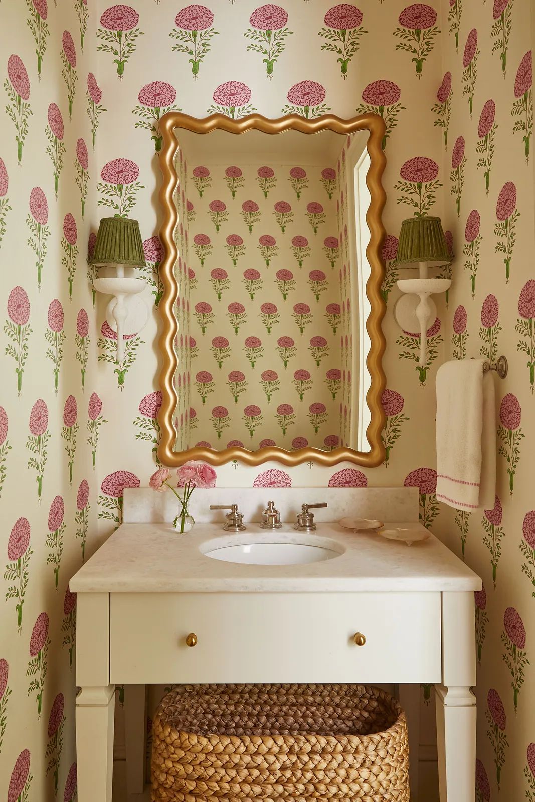 Powder room with floral wallpaper, white vanity, marble sink, gold mirror, and wall sconces.
