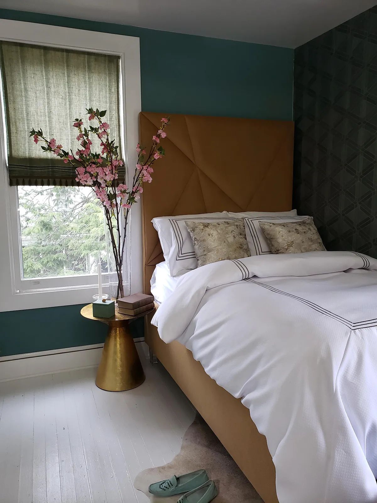 Bedroom with gold upholstered bed, white bedding, side table, and patterned wallpaper.