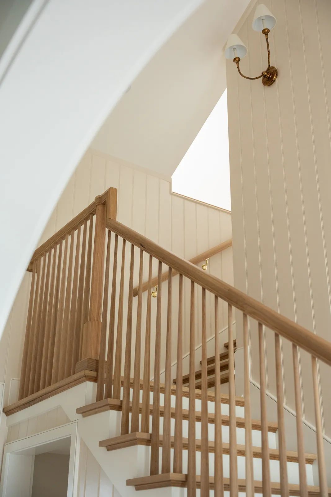 Staircase with wooden banisters, shiplap walls, and wall-mounted light fixture near skylight