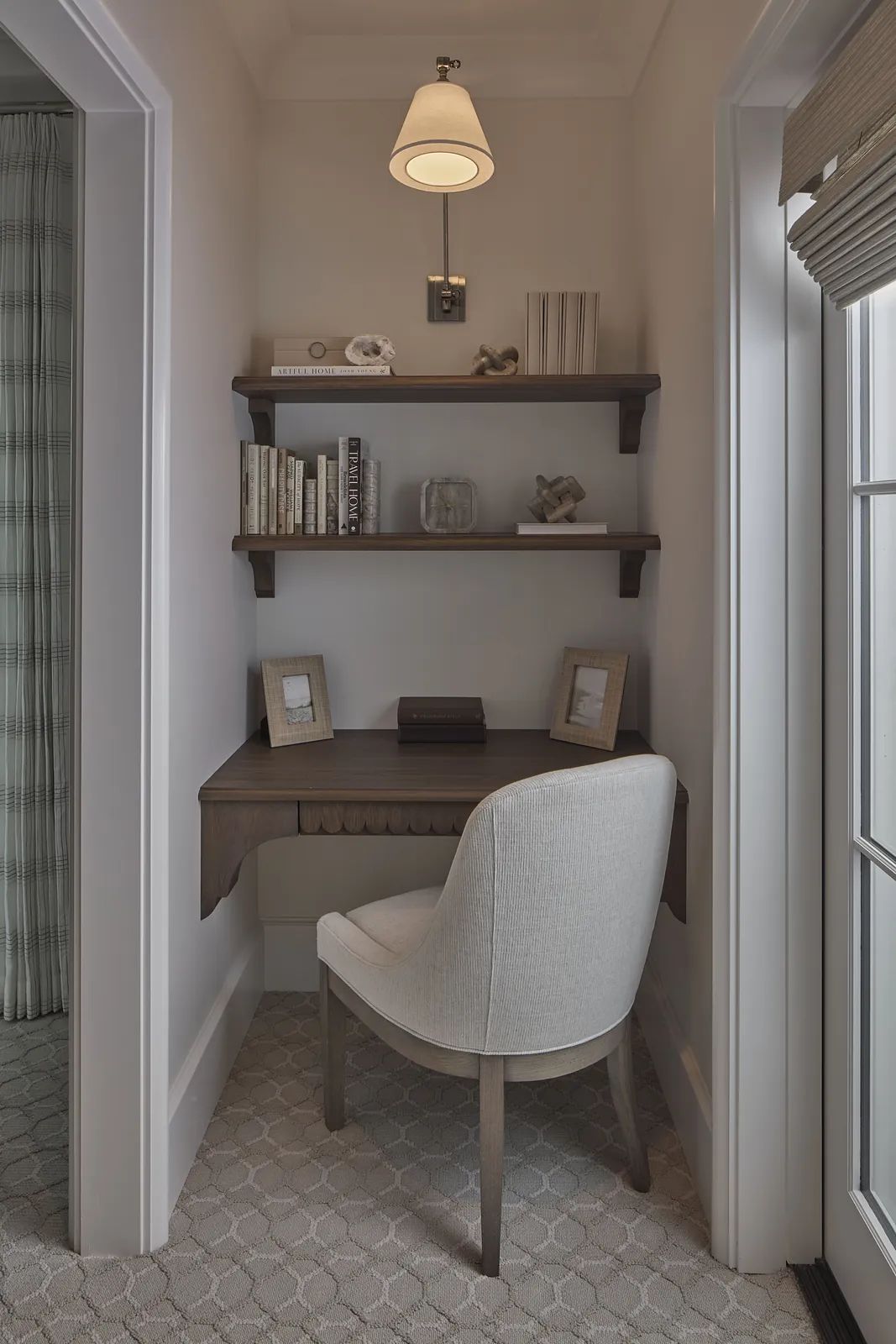 Small office with wooden desk, white chair, floating shelves, and wall sconce.