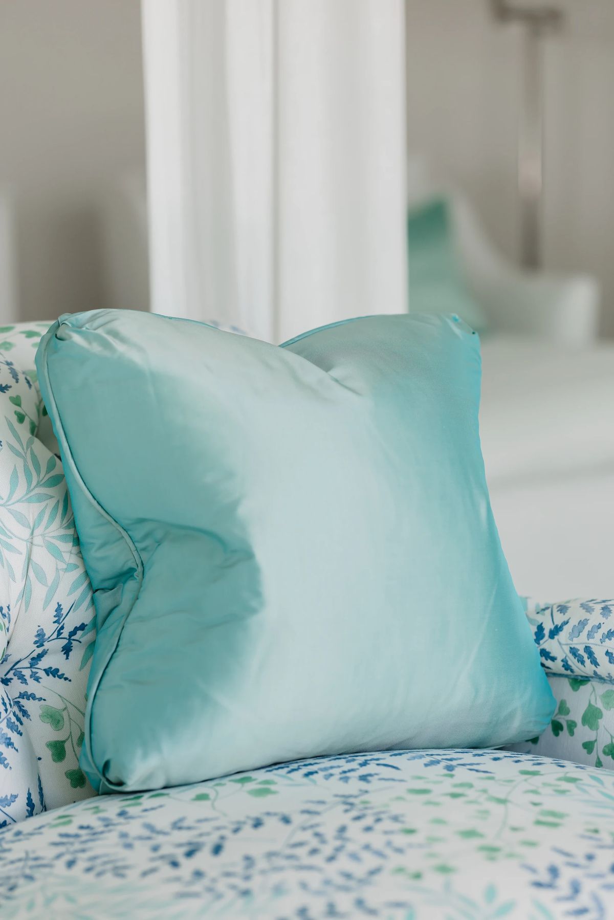 Close-up of light blue silk pillow on floral patterned chair.