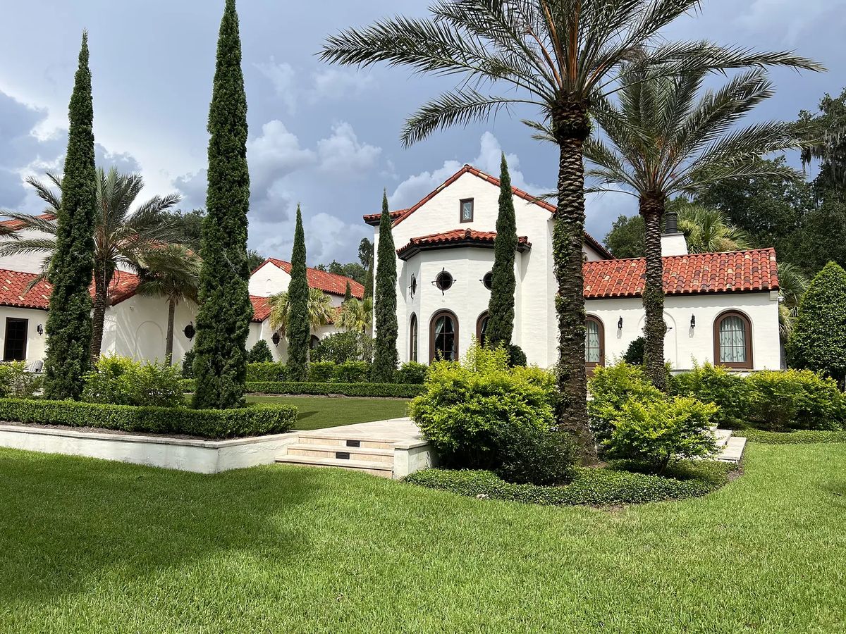 Exterior front view of a house with white stucco, red tile roof, arched windows, and landscaped lawns.