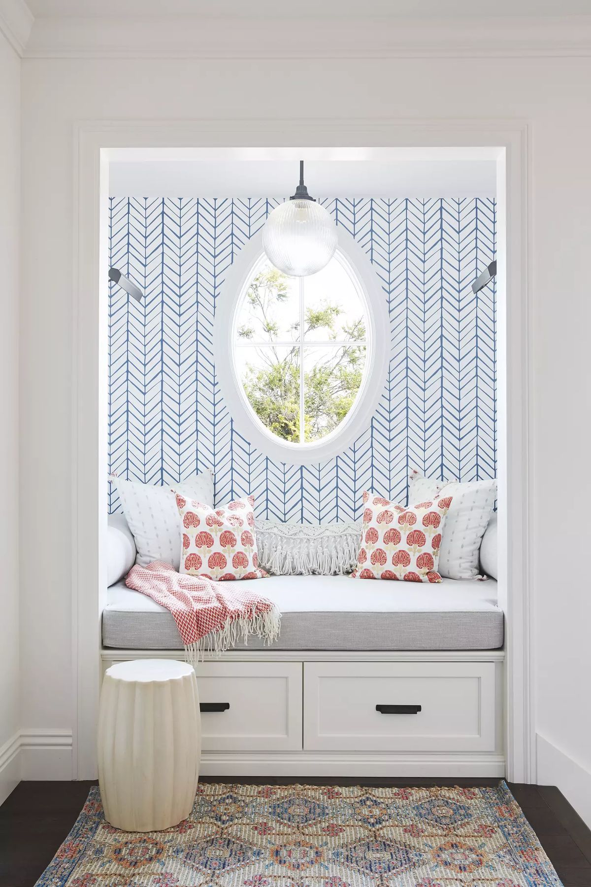 Small nook with daybed, decorative pillows, round window, and multi-colored area rug.