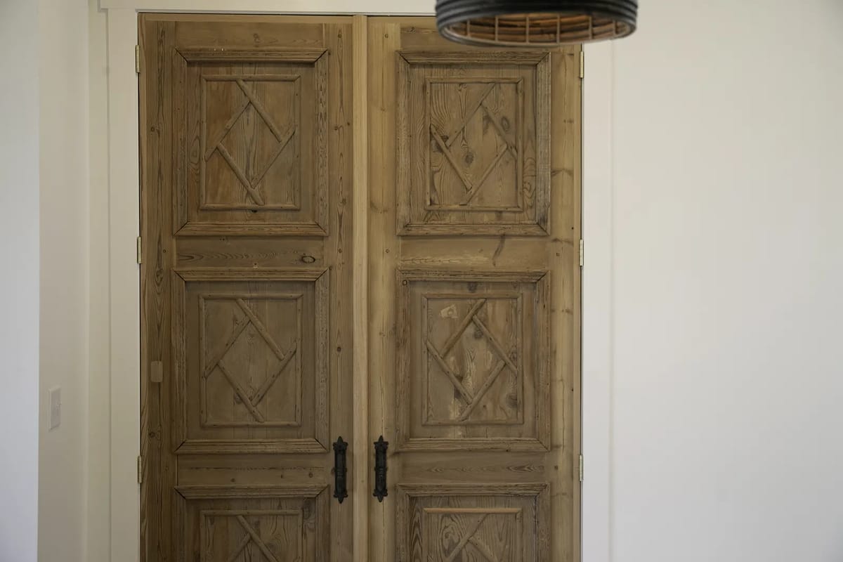 Foyer with large wooden double doors and a decorative ceiling light fixture against white walls.