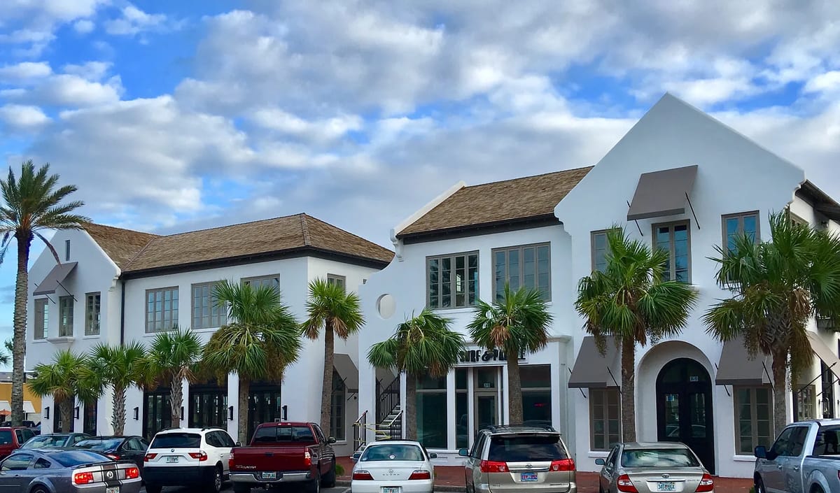 Exterior front view of a commercial building with palm trees and multiple vehicles in the parking area.