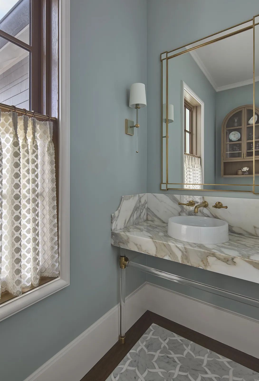 Powder room with marble sink, brass faucet, large mirror, patterned curtains, and decorative rug.