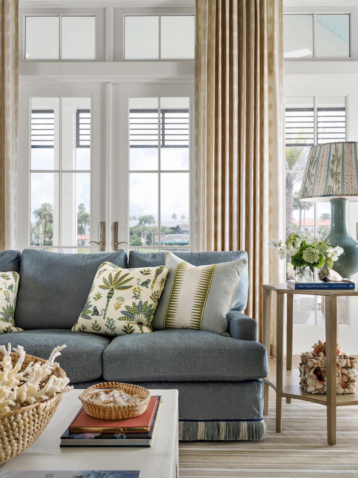 Living room with blue sofa, decorative pillows, coffee table, side table, curtains, and large glass doors.