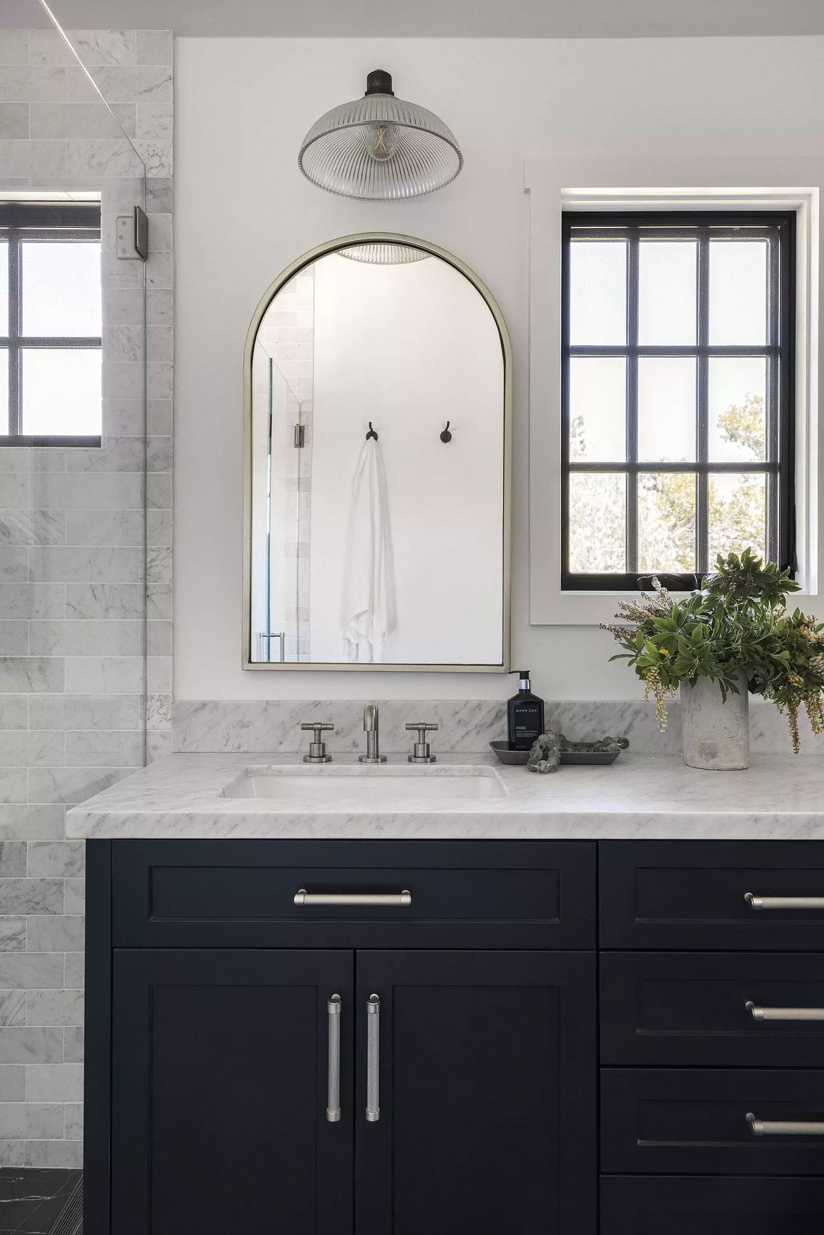 Bathroom with dark vanity, white marble countertop, arched mirror, and large window.