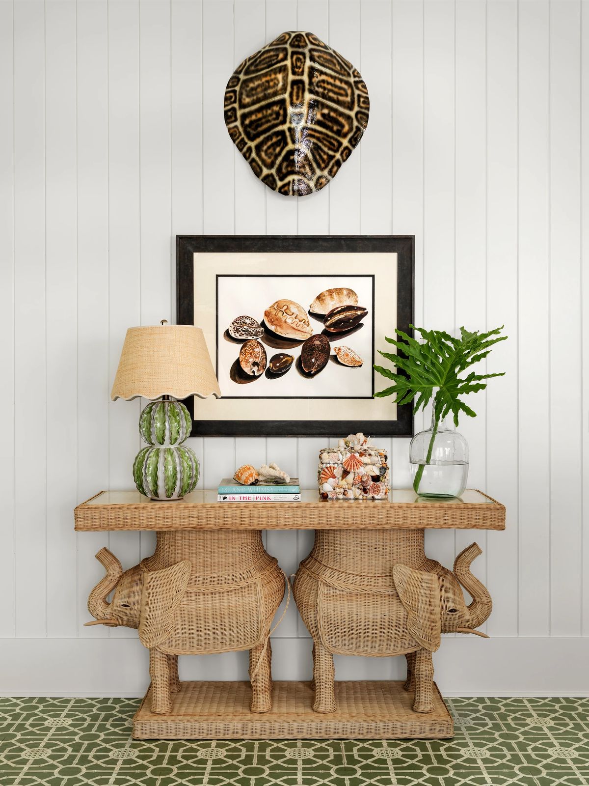 Entryway with elephant console table, lamp, plant, shell artwork, and green patterned tile floor.