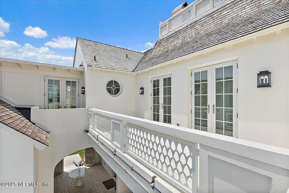 Exterior rear view with balcony, double doors, windows, and a table with chairs