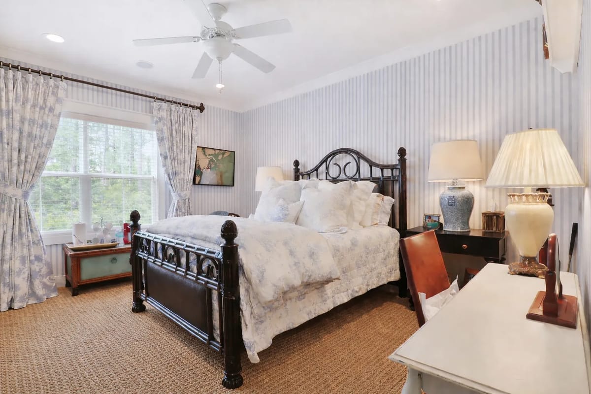 Bedroom with dark wooden bed, blue floral bedding, striped walls, and a white desk.
