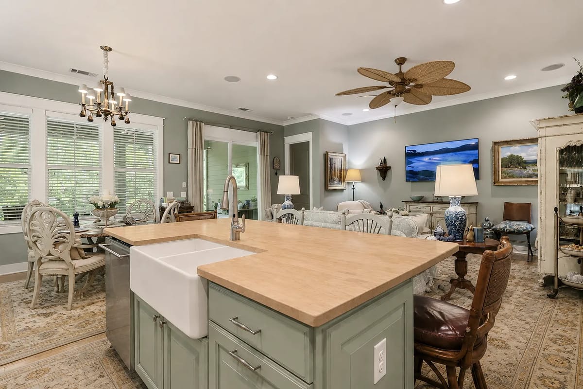 Kitchen with island, farmhouse sink, green cabinetry, dining area, and large windows for natural light