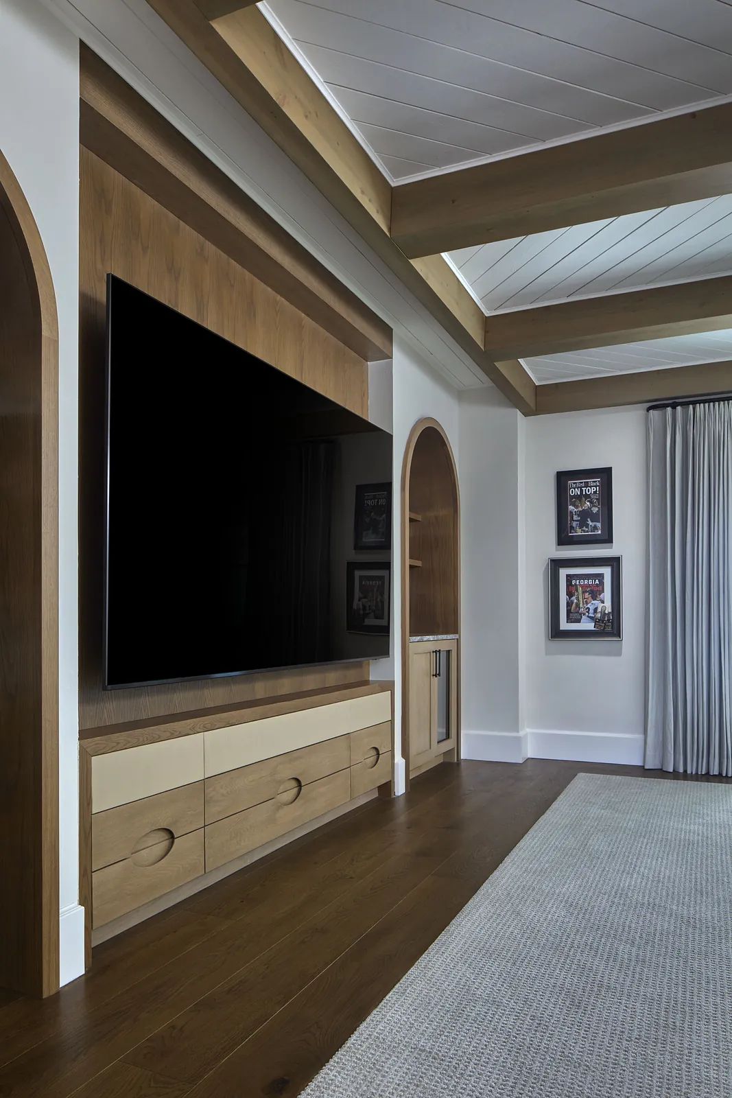 Living room with a flat-screen TV, wooden wall unit, rug, and framed pictures on light-colored walls.