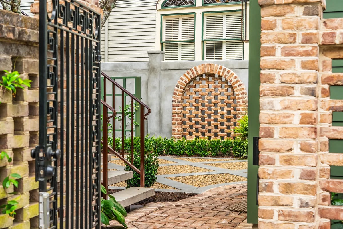 Garden with brick pathways, plants, arches, gated entrance, stone steps, and manicured shrubs.