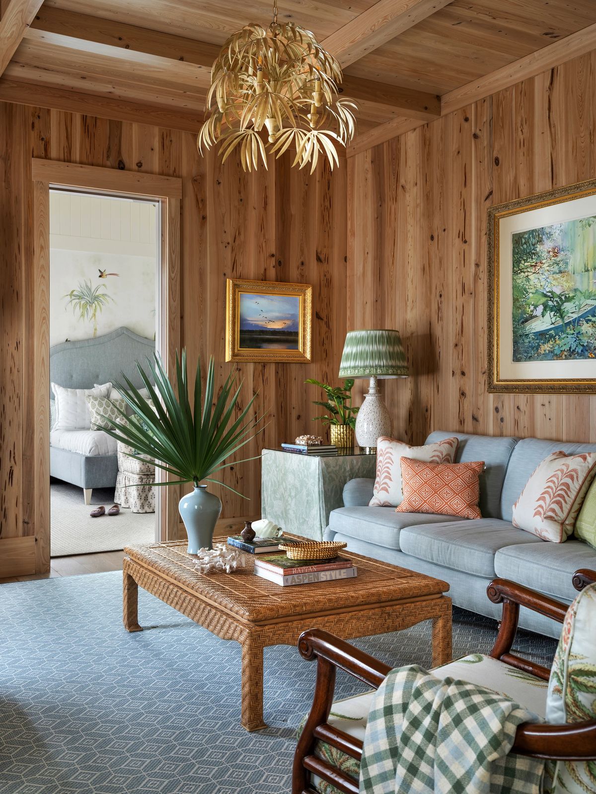 Living room with blue sofa, rattan coffee table, palm plant, decorative pillows, and wood paneled walls.
