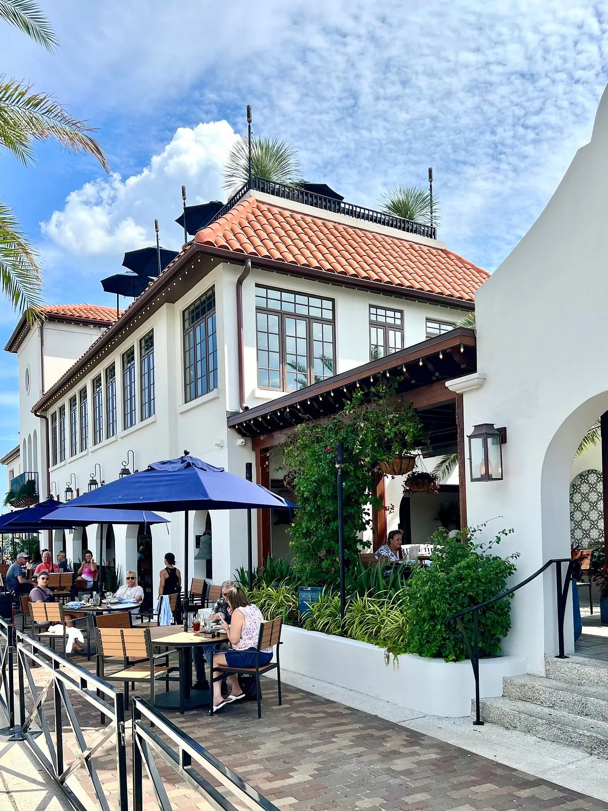 Restaurant exterior with tiled roof, large windows, outdoor seating, and decorative plants.