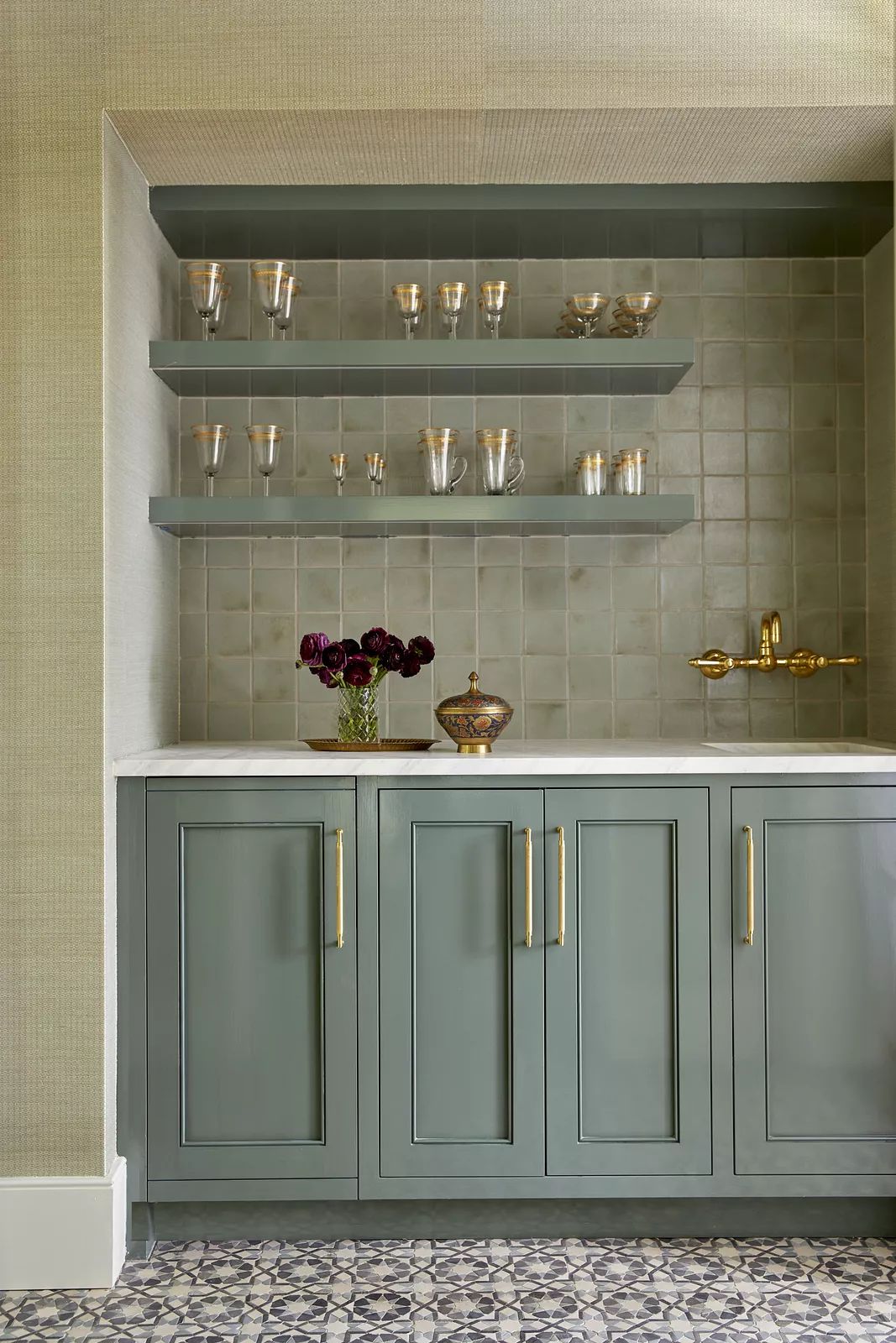 Butler's pantry with green cabinetry, white countertop, glassware, and patterned tile flooring.