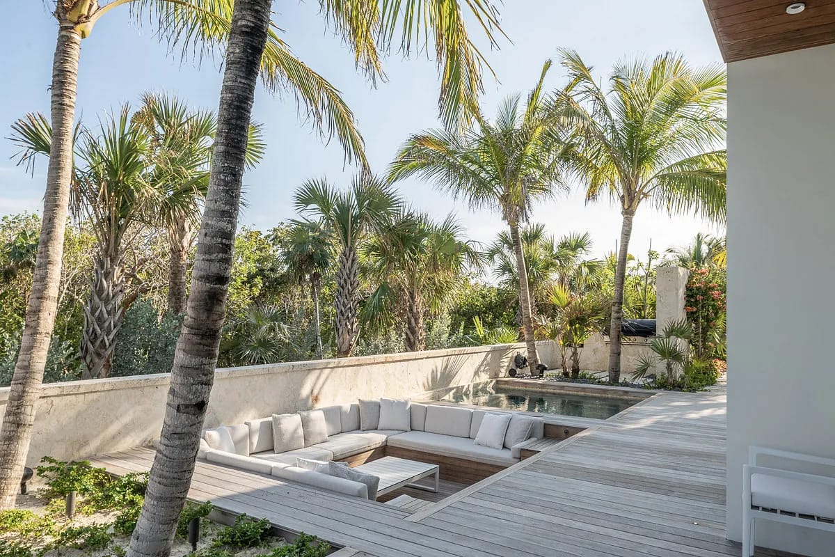 Outdoor patio with sectional sofa, coffee table, decking, pool, and tropical palm trees in the background