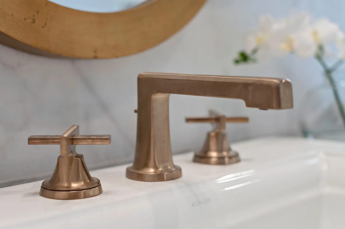 Bathroom with white bathtub, bronze faucet, marble wall, round mirror, and orchid plant