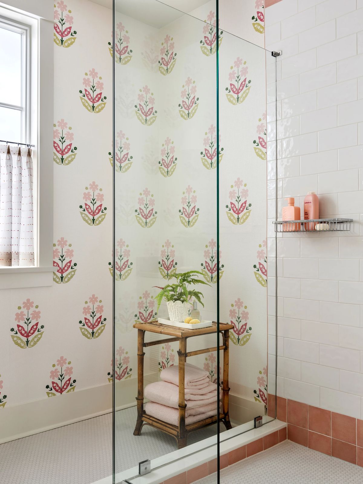 Bathroom with glass shower, floral wallpaper, white tiles, pink floor, and wooden towel stand.