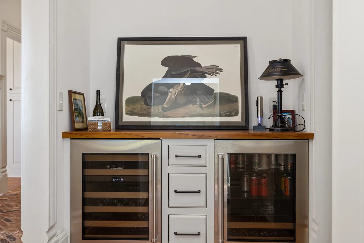 Butler's pantry with wine refrigerators, wooden countertop, artwork, table lamp, and cabinetry.