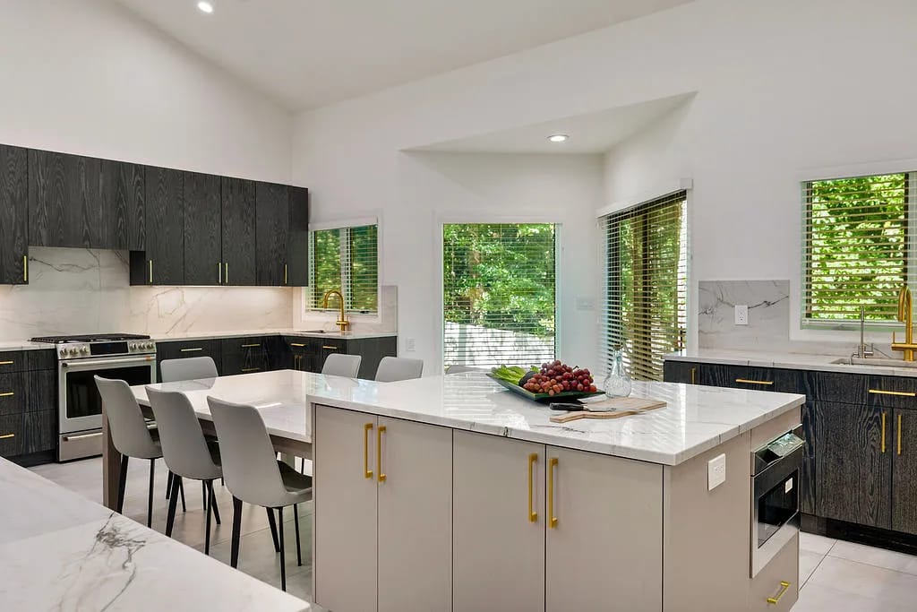 Kitchen with black cabinetry, white countertop, stainless steel appliances, dining table, and large windows